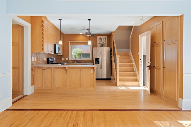 kitchen featuring kitchen peninsula, hanging light fixtures, light hardwood / wood-style flooring, stainless steel appliances, and light brown cabinets