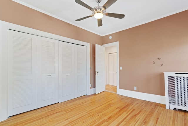 unfurnished bedroom with ceiling fan, radiator heating unit, a closet, crown molding, and hardwood / wood-style floors