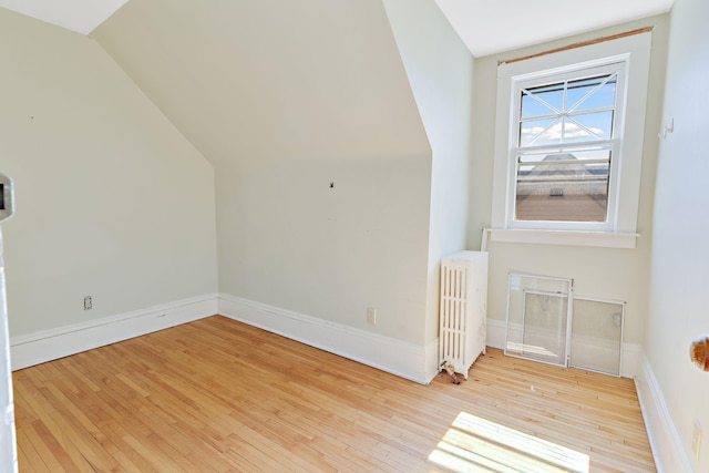 additional living space featuring light hardwood / wood-style floors, lofted ceiling, and radiator