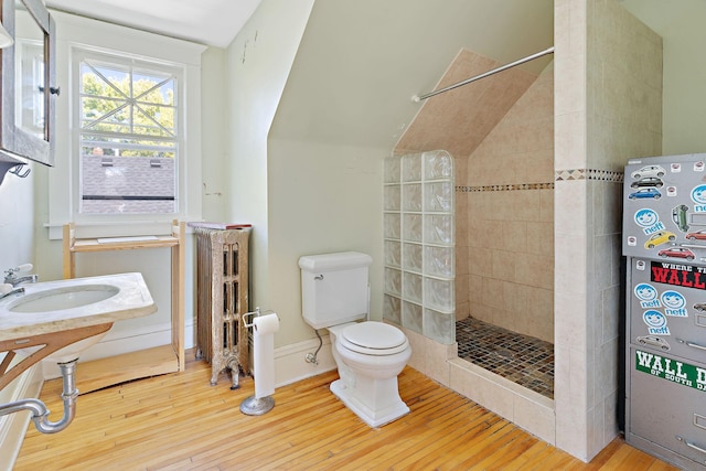 bathroom with hardwood / wood-style floors, tiled shower, and toilet