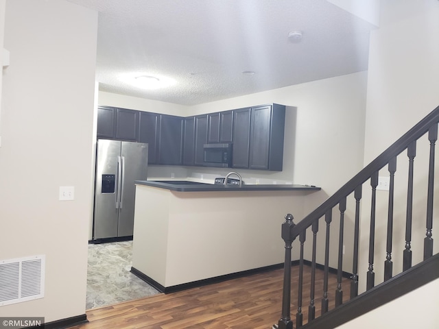 kitchen featuring appliances with stainless steel finishes, blue cabinets, kitchen peninsula, a textured ceiling, and hardwood / wood-style floors