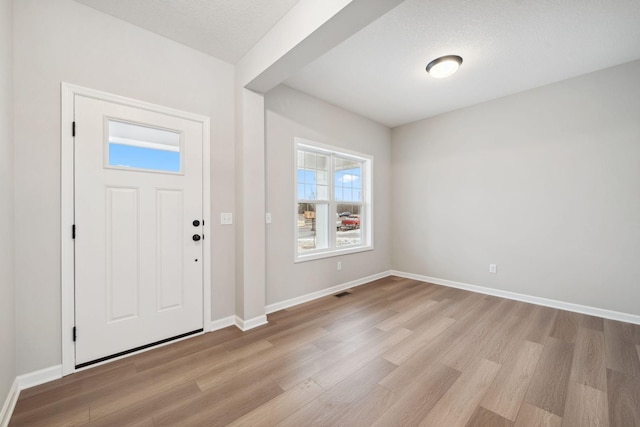 entryway featuring visible vents, baseboards, light wood-type flooring, and a textured ceiling