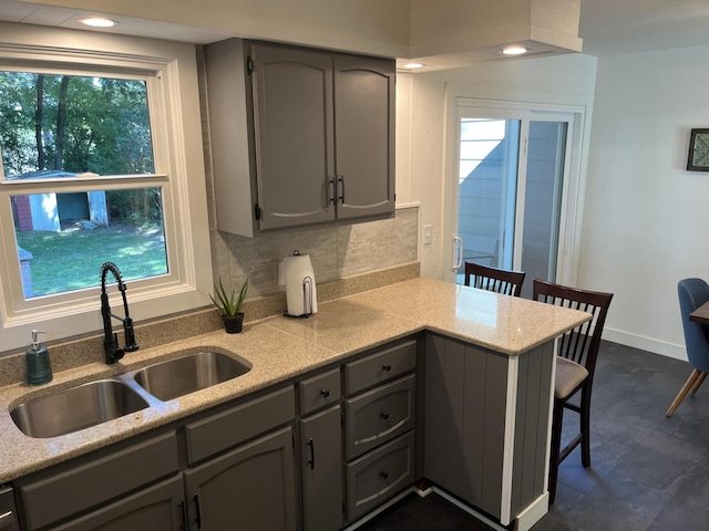 kitchen with gray cabinetry, kitchen peninsula, a kitchen bar, sink, and tasteful backsplash