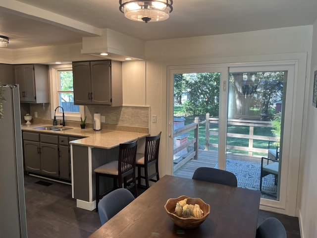 kitchen featuring a breakfast bar area, gray cabinetry, stainless steel fridge, decorative backsplash, and sink