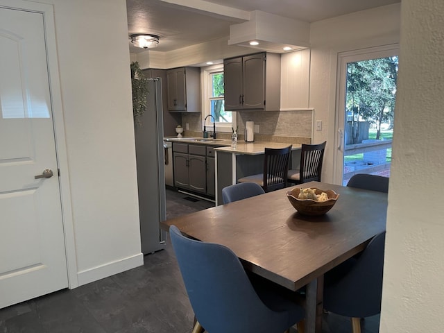 kitchen with gray cabinets, stainless steel refrigerator, a kitchen bar, decorative backsplash, and sink