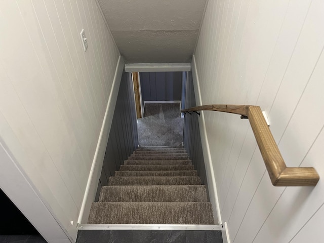 stairs with a textured ceiling and wooden walls