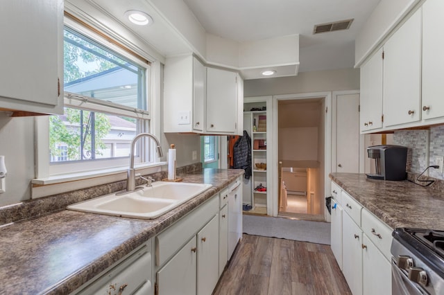 kitchen featuring dark hardwood / wood-style flooring, sink, stainless steel range oven, decorative backsplash, and white cabinetry