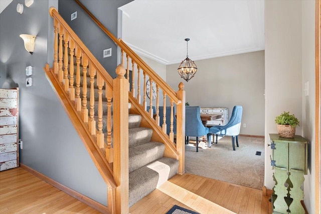 stairway with an inviting chandelier, ornamental molding, and hardwood / wood-style floors