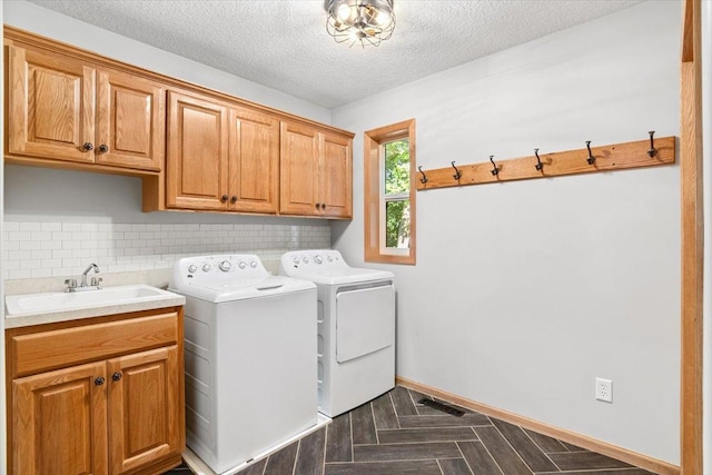 clothes washing area with dark parquet floors, sink, a textured ceiling, cabinets, and independent washer and dryer