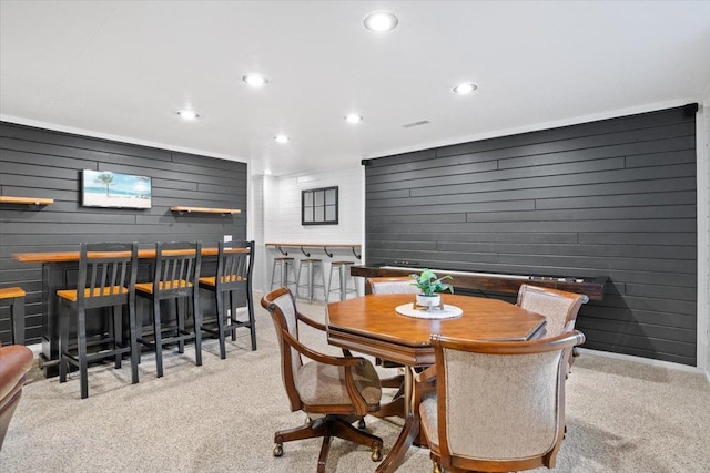 dining space featuring bar area, light colored carpet, and wood walls