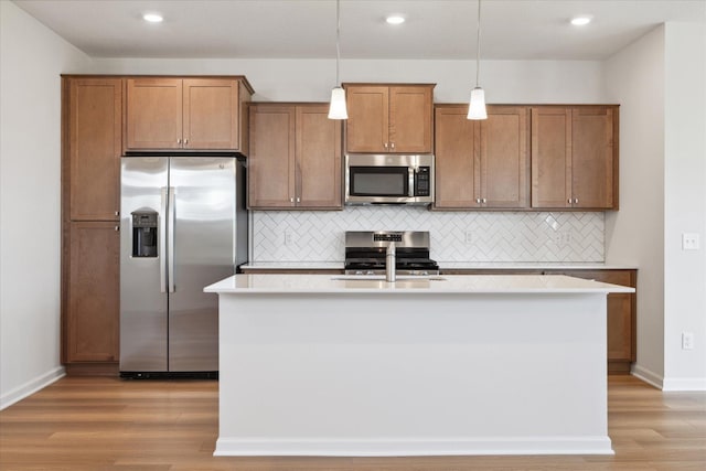 kitchen featuring an island with sink, appliances with stainless steel finishes, backsplash, light wood-type flooring, and pendant lighting