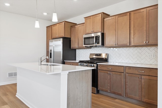 kitchen featuring sink, tasteful backsplash, hanging light fixtures, an island with sink, and stainless steel appliances