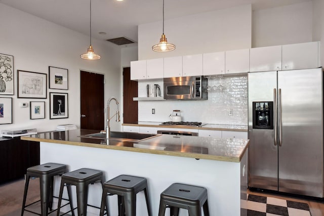 kitchen with white cabinetry, stainless steel appliances, a kitchen island with sink, and hanging light fixtures