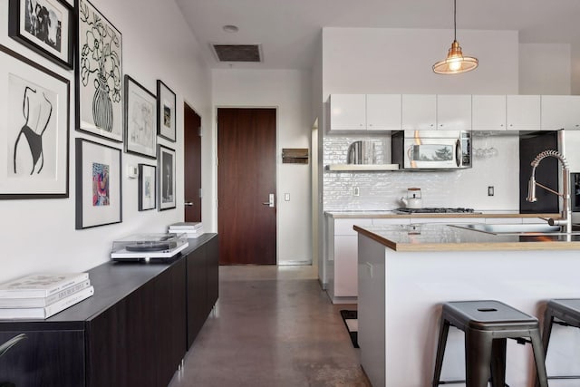 kitchen with pendant lighting, a kitchen bar, white cabinets, and appliances with stainless steel finishes