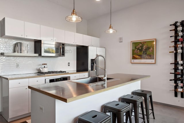 kitchen featuring a breakfast bar, white cabinetry, decorative light fixtures, stainless steel appliances, and a kitchen island with sink