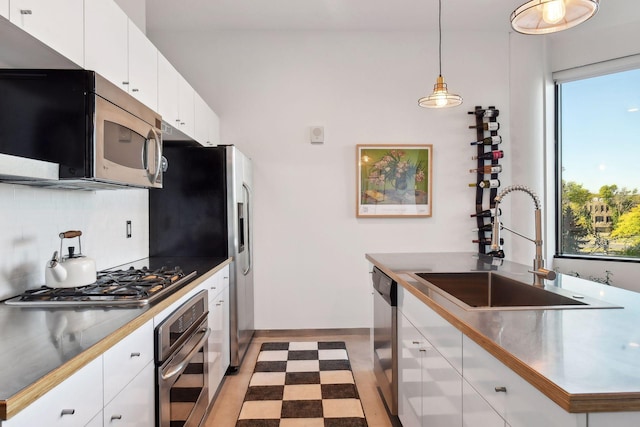 kitchen with appliances with stainless steel finishes, pendant lighting, sink, white cabinets, and backsplash