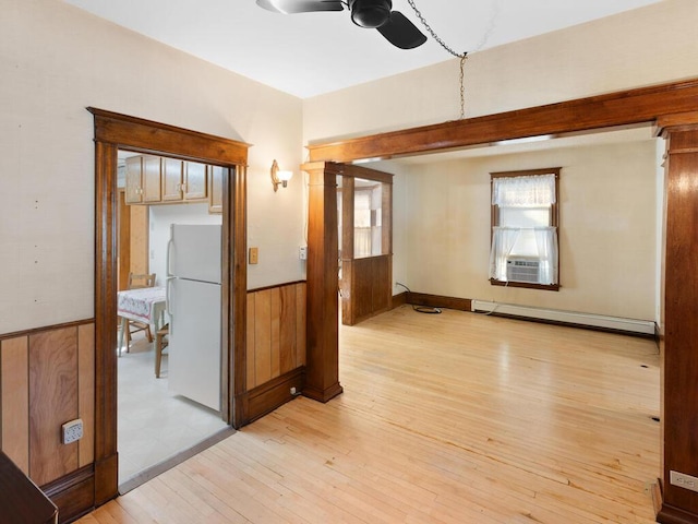 spare room featuring wood walls, decorative columns, a baseboard heating unit, ceiling fan, and light hardwood / wood-style flooring