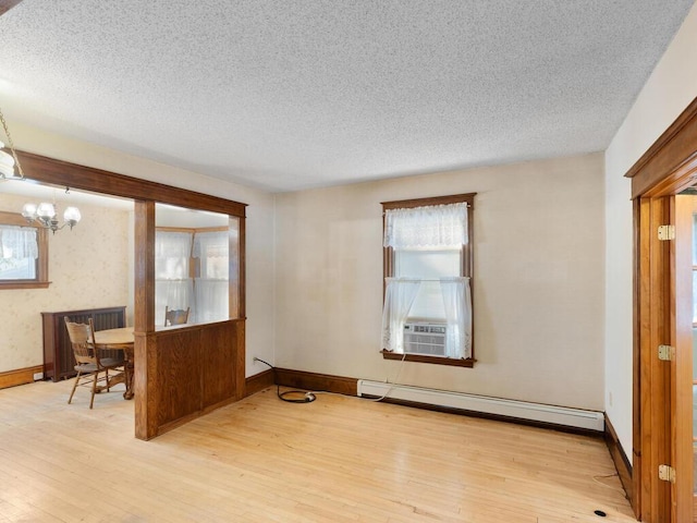 unfurnished room with light hardwood / wood-style floors, baseboard heating, a textured ceiling, and a notable chandelier