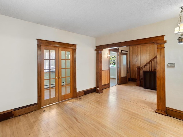 unfurnished room featuring light wood-type flooring, ornate columns, a baseboard heating unit, and french doors