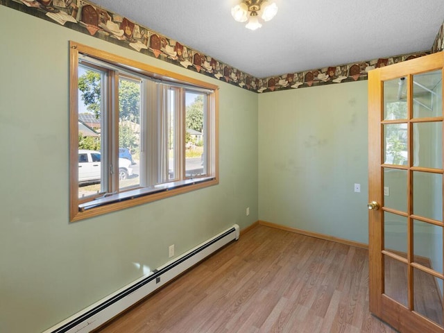 empty room with a textured ceiling, light hardwood / wood-style floors, and a baseboard radiator