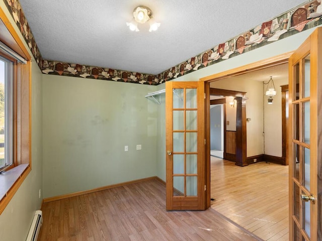 unfurnished room featuring hardwood / wood-style floors, french doors, a textured ceiling, and a baseboard radiator