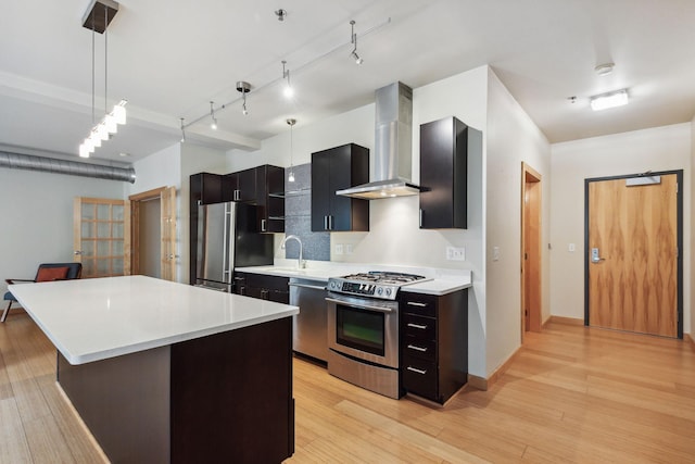 kitchen featuring a center island, hanging light fixtures, wall chimney exhaust hood, stainless steel appliances, and light hardwood / wood-style flooring