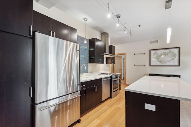 kitchen featuring pendant lighting, sink, wall chimney exhaust hood, light hardwood / wood-style flooring, and appliances with stainless steel finishes