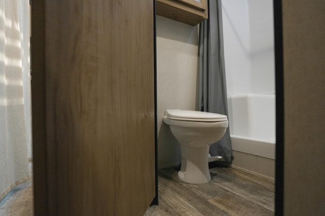 bathroom with hardwood / wood-style floors, toilet, and shower / bath combination with curtain