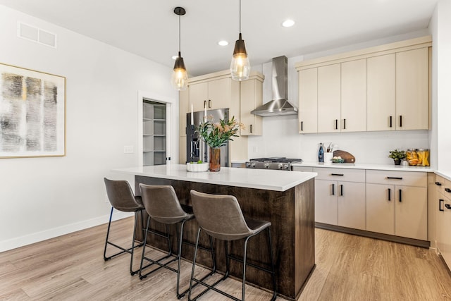 kitchen featuring stainless steel fridge with ice dispenser, wall chimney range hood, cream cabinetry, and a center island