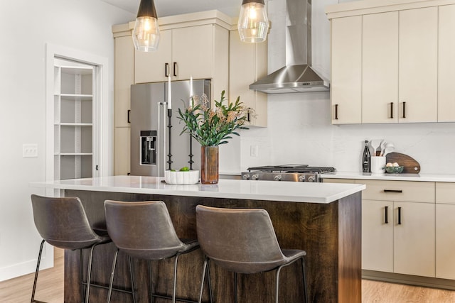 kitchen featuring wall chimney exhaust hood, high end refrigerator, a center island, light hardwood / wood-style floors, and cream cabinetry