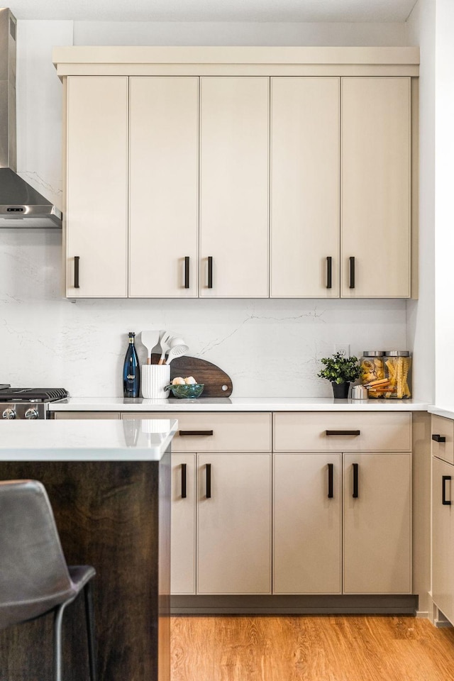 bar featuring cream cabinetry, light wood-type flooring, and wall chimney range hood