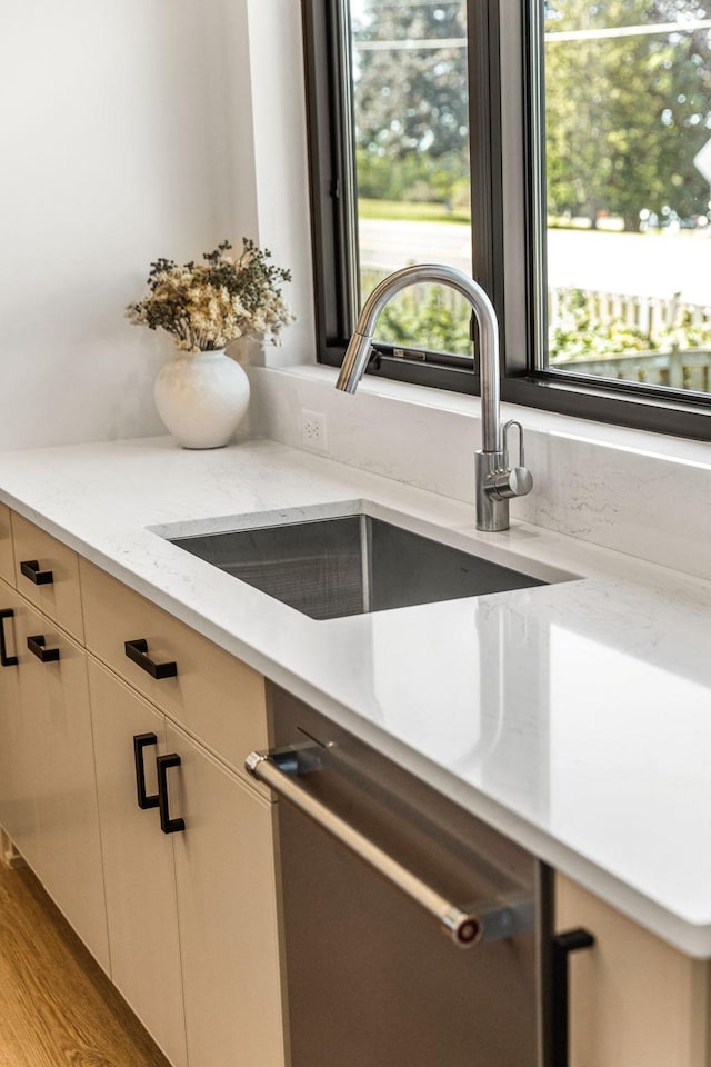 interior details featuring stainless steel dishwasher, light stone countertops, sink, and white cabinets