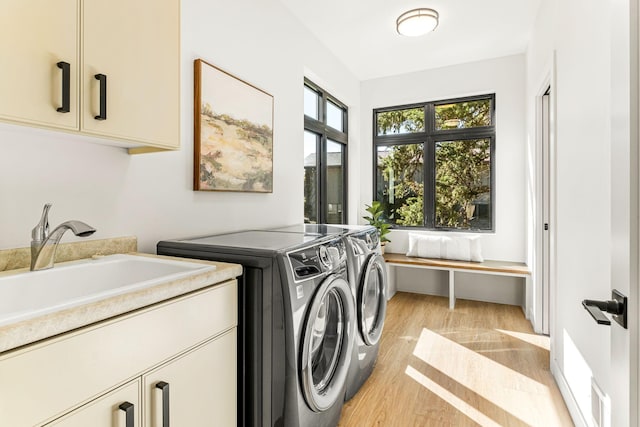 laundry room with cabinets, sink, washer and dryer, and light wood-type flooring