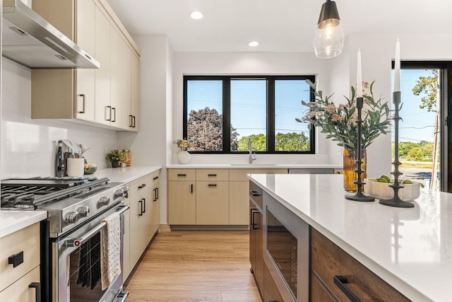 kitchen with sink, hanging light fixtures, gas range, cream cabinets, and wall chimney range hood