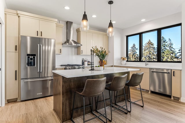 kitchen with appliances with stainless steel finishes, light countertops, light wood-style flooring, and wall chimney exhaust hood