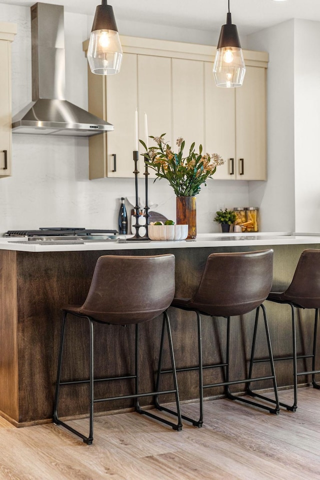 kitchen featuring light wood-type flooring, wall chimney exhaust hood, a kitchen breakfast bar, and hanging light fixtures