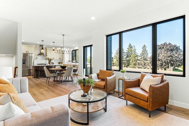 living area featuring baseboards, light wood-type flooring, a chandelier, and recessed lighting