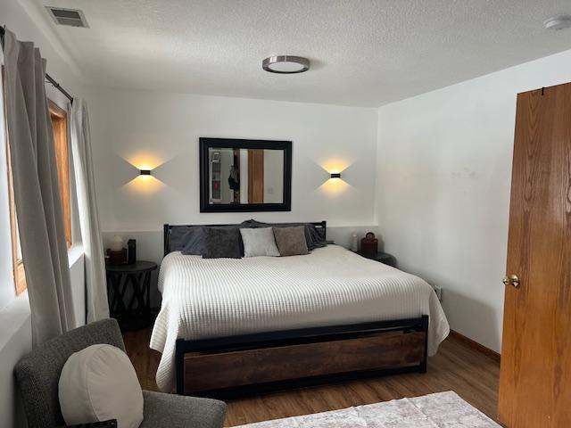 bedroom featuring visible vents, a textured ceiling, and wood finished floors