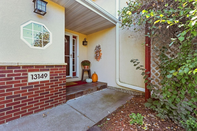 view of exterior entry featuring stucco siding and brick siding