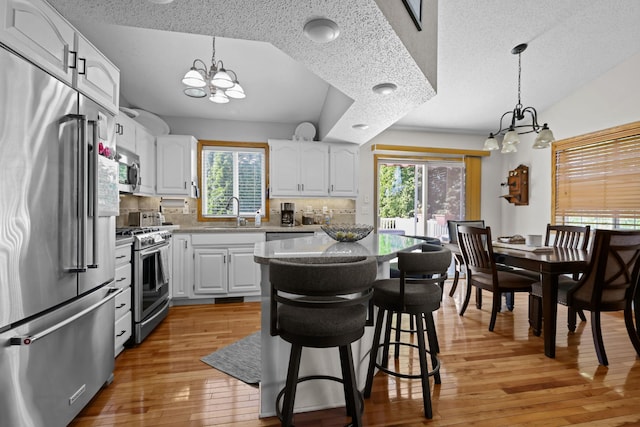 kitchen with backsplash, a center island, stainless steel appliances, light wood finished floors, and a chandelier