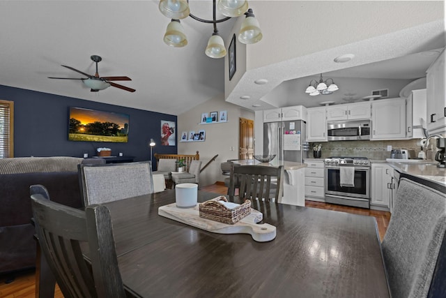 dining space featuring ceiling fan with notable chandelier, vaulted ceiling, and wood finished floors