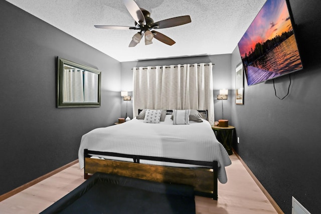 bedroom featuring ceiling fan, a textured ceiling, baseboards, and wood finished floors