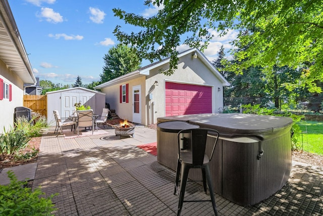 view of patio / terrace featuring a hot tub, an outdoor fire pit, a fenced backyard, a garage, and an outdoor structure