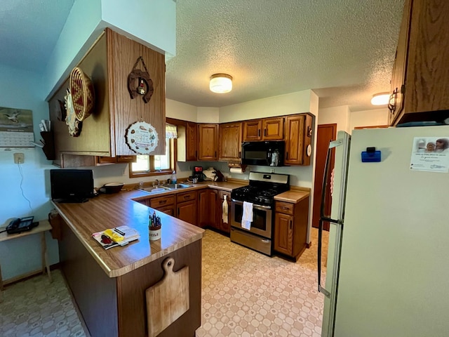 kitchen with a textured ceiling, kitchen peninsula, stainless steel gas range oven, and white fridge