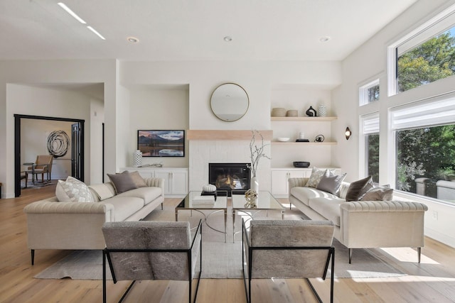 living area with light wood-style floors, a tiled fireplace, recessed lighting, and built in shelves