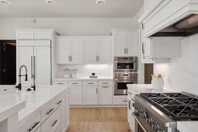 kitchen with light stone counters, light wood finished floors, custom range hood, high quality appliances, and white cabinets