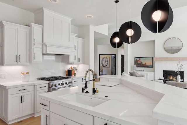 kitchen with a sink, high end stove, open floor plan, and white cabinets