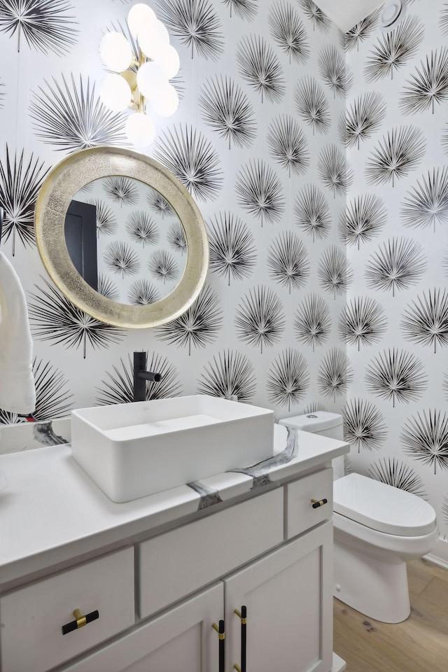 half bath with toilet, vanity, a chandelier, and wood finished floors