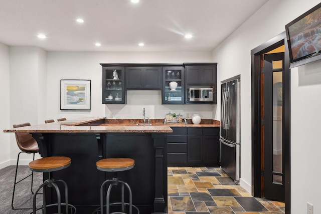kitchen with a sink, stainless steel appliances, a breakfast bar area, glass insert cabinets, and baseboards