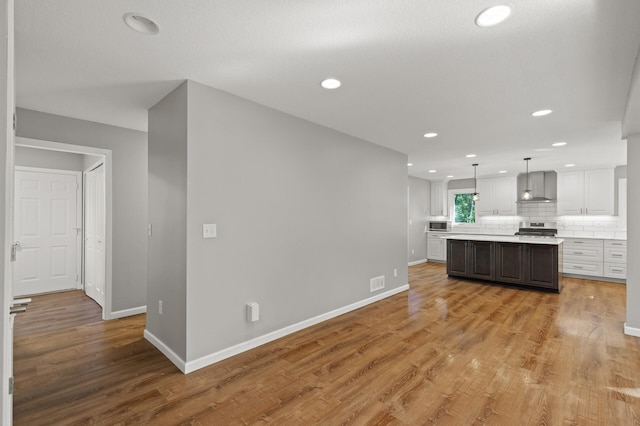 kitchen featuring pendant lighting, a kitchen island, wall chimney range hood, white cabinetry, and stainless steel appliances